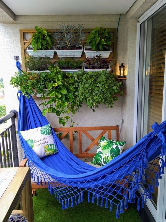 Small balcony with a bold blue hammock, potted herbs, and simple wooden furniture
