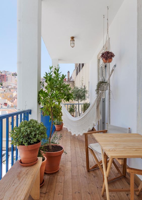 Boho balcony with wooden furniture, potted greenery, and a white hammock with detailing
